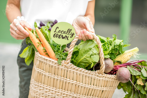 Holding bag full of fresh organic vegetables with green sticker from the local market on the green background