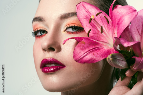 close-up portrait of beautiful young woman with stylish makeup and pink lilium flowers isolated on white