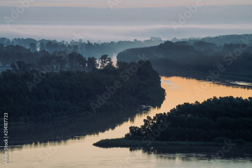 Early blue sky reflected in river water. Riverbank with forest under predawn sky. Cloudy sky on background. Fog hid trees on island. Colorful morning atmospheric landscape of majestic nature. photo