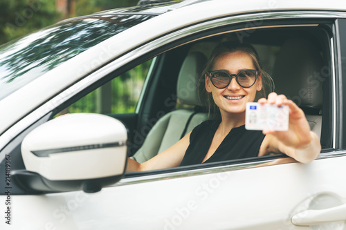 happy young woman showing her driver license through the car window photo