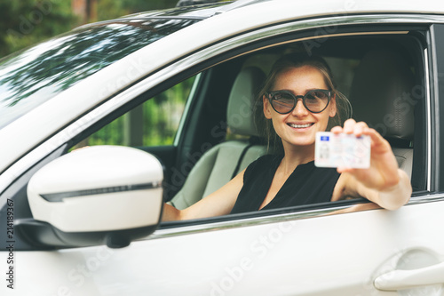 happy young woman showing her driver license through the car window © ronstik