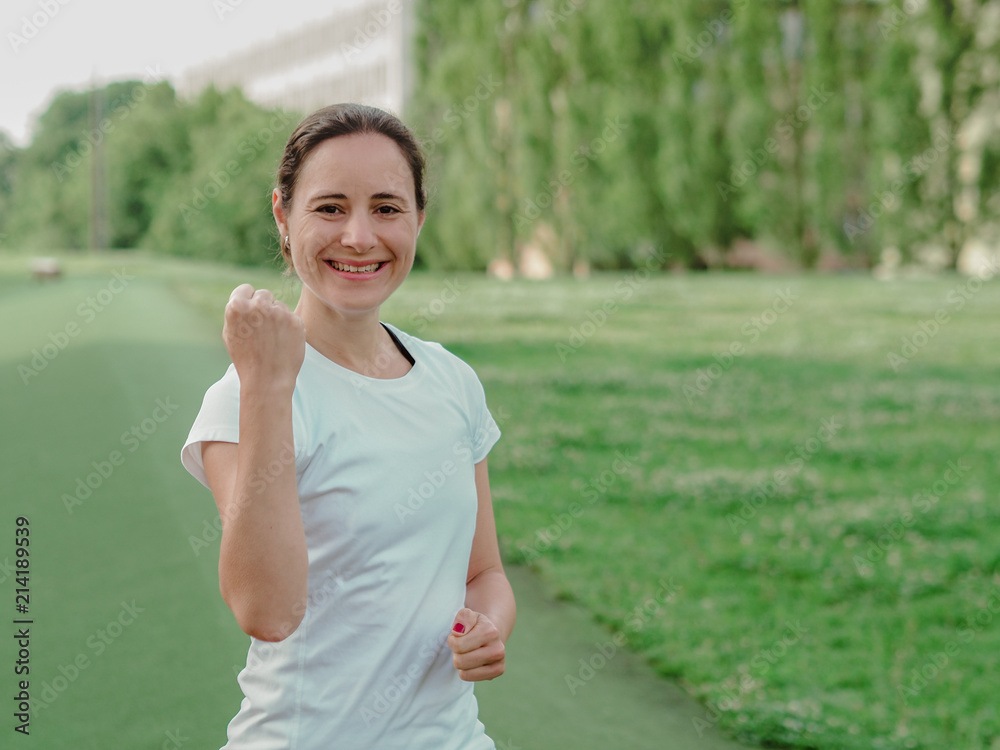 happy smiling femal Fitness Coach in white sportswear making fists outside in the park happy smiling femal Fitness Coach in white sportswear making fists outside in the park