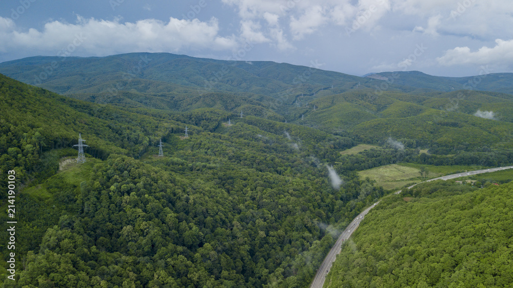 Aerial stock photo of car driving along the winding mountain pass road through the forest in Sochi, Russia. People traveling, road trip on curvy road through beautiful countryside scenery.