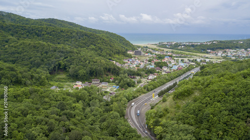 Aerial stock photo of car driving along the winding mountain pass road through the forest in Sochi, Russia. People traveling, road trip on curvy road through beautiful countryside scenery.