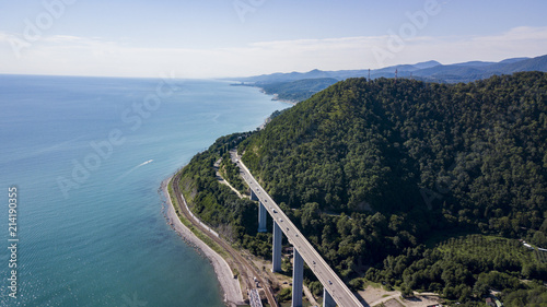 Aerial stock photo of car driving along the winding mountain pass road through the forest in Krasnodar Krai, Russia. People traveling, road trip on curvy road through beautiful countryside scenery.