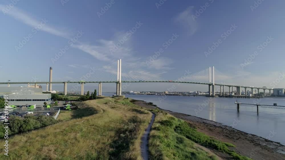 Drone moves backwards over grass river bank with Queen Elizabeth II Bridge in background Drone moves backwards over grass river bank with Queen Elizabeth II Bridge in background