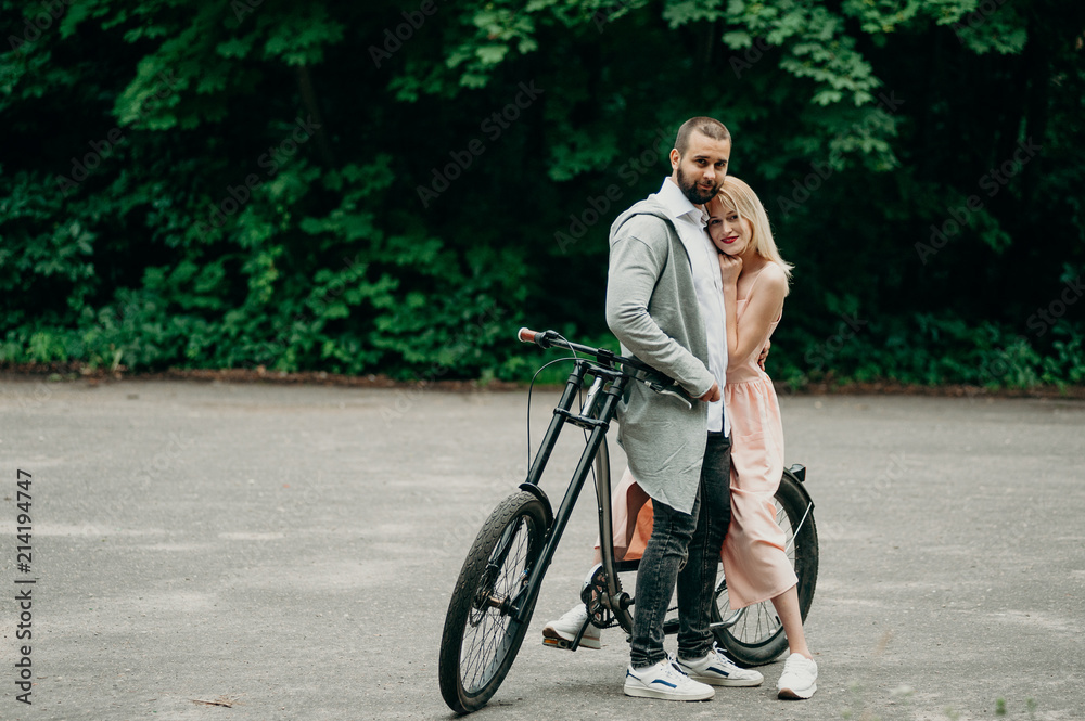 Smiling couple hugging near the modern bicycle in park. Love and tenderness, dating, romance. Lifestyle concept