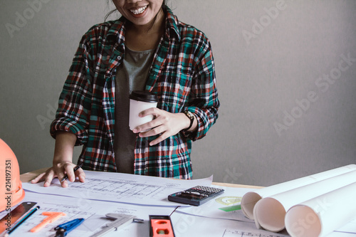 Concept architects,woman engineer smiling holding cup of coffee looking architects On the desk with a blueprint in the office. photo