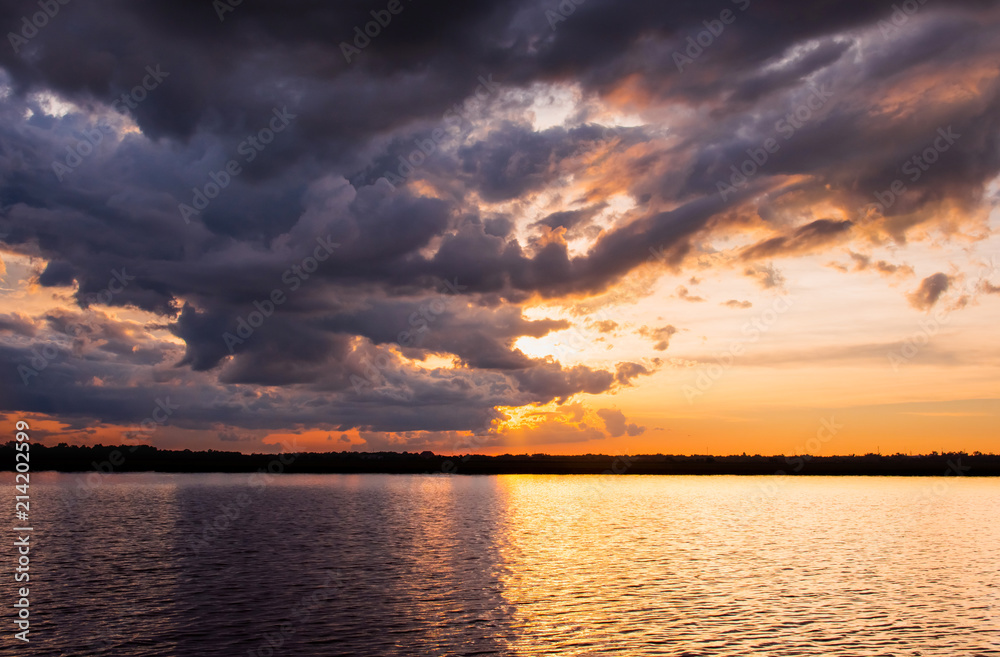 Sunset in the lake. Beautiful sunset behind the storm clouds before a thunder storm above the over lake landscape background. Dramatic sky with cloud at sunset.