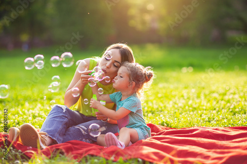 Family in park -Female child blows soup foam and make bubbles with her mother in nature.