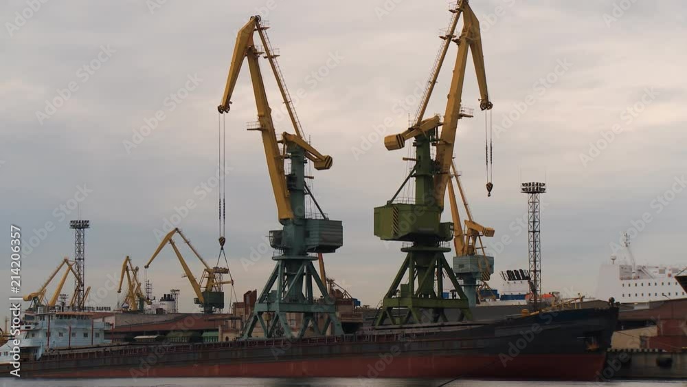The port crane unloads the cargo ship at the pier against the backdrop of the port infrastructure The port crane unloads the cargo ship at the pier against the backdrop of the port infrastructure