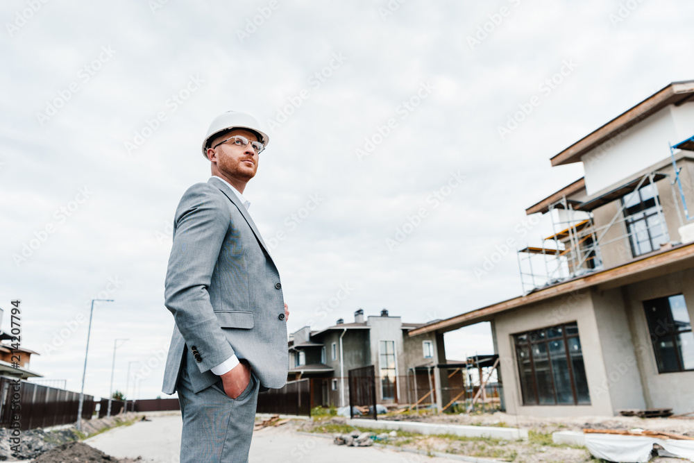 successful architect in suit and hard hat standing in front of building house