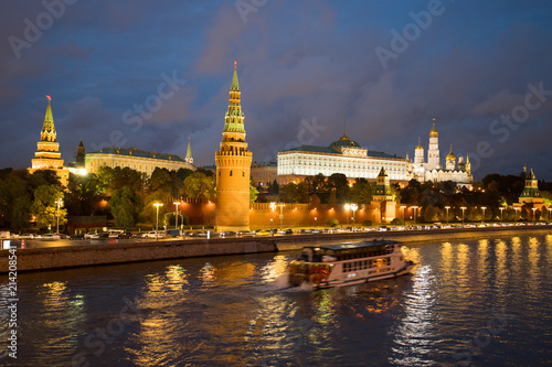 Moscow, Russia. Beautiful View On Moscow Kremlin With Illuminations From Lamps And With Floating Motor Ship On Coast Of Moscow River Under Blue Dramatic Sky In Evening Day In Autumn.