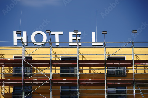 Gerüst vor der Hotelfassade / Eine Hotelfassade mit Schild wird renoviert und eine Baugerüst steht davor.