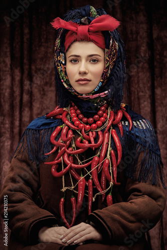 Fotografie Portrait of young pretty woman sitting in ethnic winter costume with hands on he