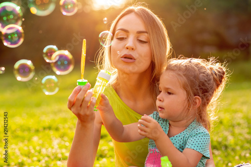 family, happiness, childhood and people concept - Female child blows soup foam and make bubbles with her mother in park.