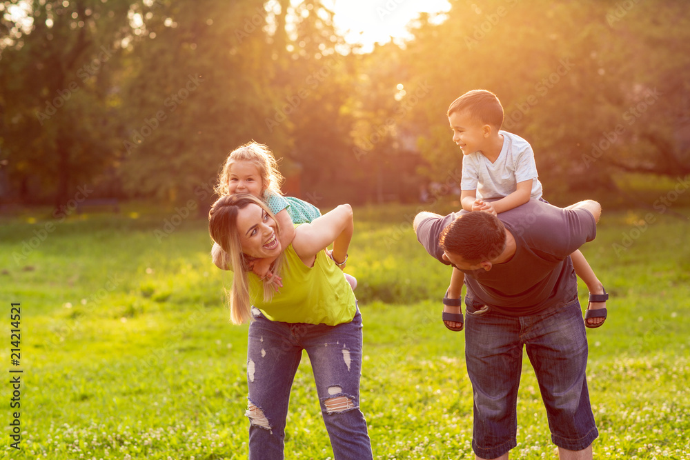 Fototapeta premium family, happiness, childhood and people concept - Parents giving piggyback ride to children.
