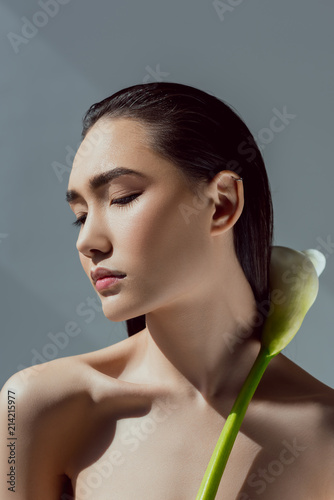 tender asian girl with closed eyes holding calla flower, isolated on grey