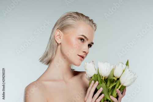 portrait of nude blonde girl posing with tulip flowers  isolated on grey