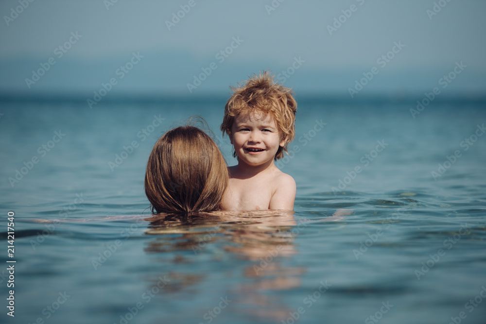 Boy is swimming in sea. Funny emotions from child during vacations. Mother swim in sea with her son. Cute blond kid hold on his mother. Family holiday together. Boy enjoys life on summer beach Boy is swimming in sea. Funny emotions from child during vacations. Mother swim in sea with her son. Cute blond kid hold on his mother. Family holiday together. Boy enjoys life on summer beach