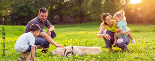 happy family is having fun with golden retriever - family playing with dog in park.