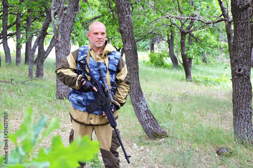 On the hunt. A man of 35-40 years old, a military hunter is standing with a firearm in the forest.