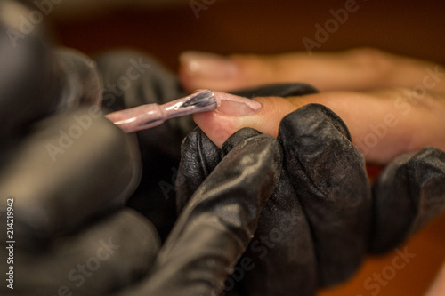 The master of nail extensions makes a hardware manicure and covers the nails with gel varnish in the beauty salon