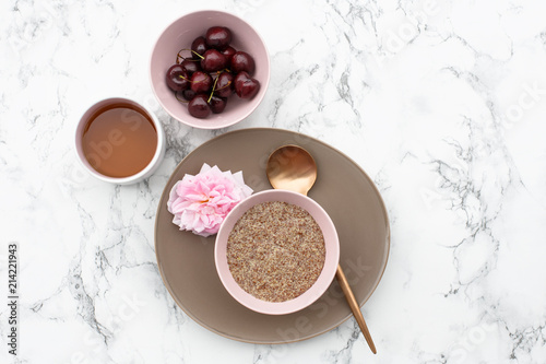 The concept of a healthy gluten-free Breakfast  linen porridge in a pink plate  herbal tea and cherries on a marble table.