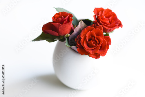 Red roses/white vase on a white background with three red roses.