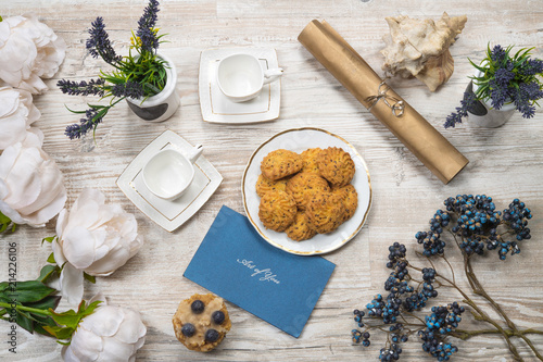 Beautiful bright tea set up with cookies and flowers. White ceramic tea pots and sweet cookies, on top of the wood table.