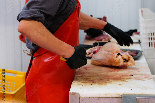 Butcher in red apron chopping poultry meat. Cutting shop of farm market.