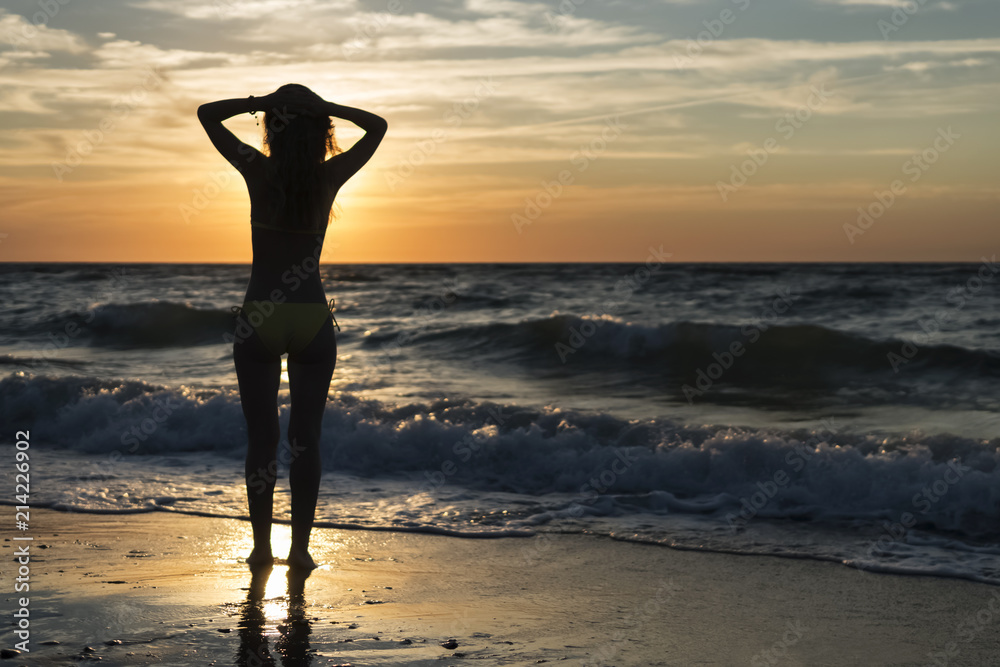 Woman is standing by the water at sunset near the stormy sea