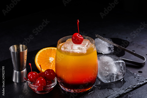 Tequila Sunrise cocktail on a wet black slate tray. Cocktail preparation set on a stone table with space for your text. photo