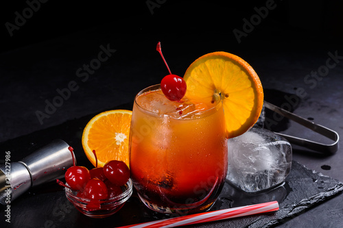 Tequila Sunrise cocktail on a wet black slate tray. Cocktail preparation set on a stone table with space for your text. photo