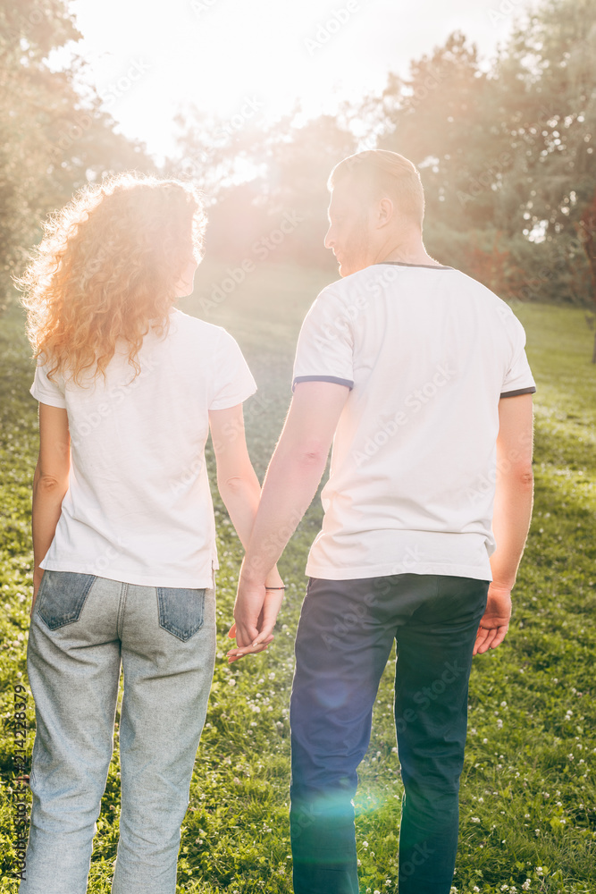 back view of young redhead couple holding hands and walking together at park