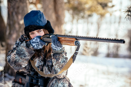 female hunter in camouflage clothes ready to hunt, holding gun and walking in forest. hunting and people concept