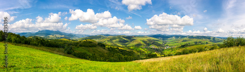 panorama of mountainous countryside. lovely countryside scenery in early autumn with grassy field on hillside, village down in the valley and clouds on a blue sky over the distant ridge