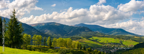 Fototapeta Naklejka Na Ścianę i Meble -  panorama of mountainous urban area. lovely countryside landscape in early autumn. trees along the road down the hill. village down in the valley and clouds on a blue sky over the distant ridge