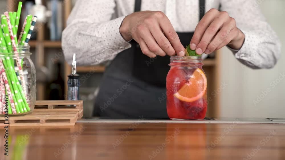 Close-up of a handsome young bartender hands finishing making a fresh, cool red color lemonade at the bar counter. Close-up of a handsome young bartender hands finishing making a fresh, cool red color lemonade at the bar counter.