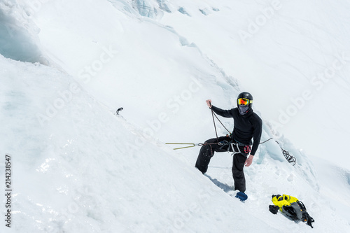 A professional mountaineer in a helmet and ski mask on the insurance does notch the ice ax in the glacier. The work of a professional climber in winter on a glacier against the blue sky