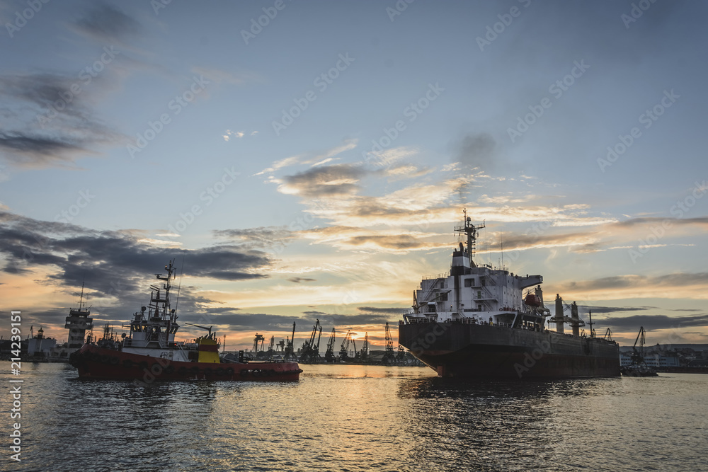 Obraz premium Tug boat entering the harbor with big cargo boat.