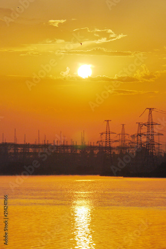 yellow sunset over the water against a power plant background