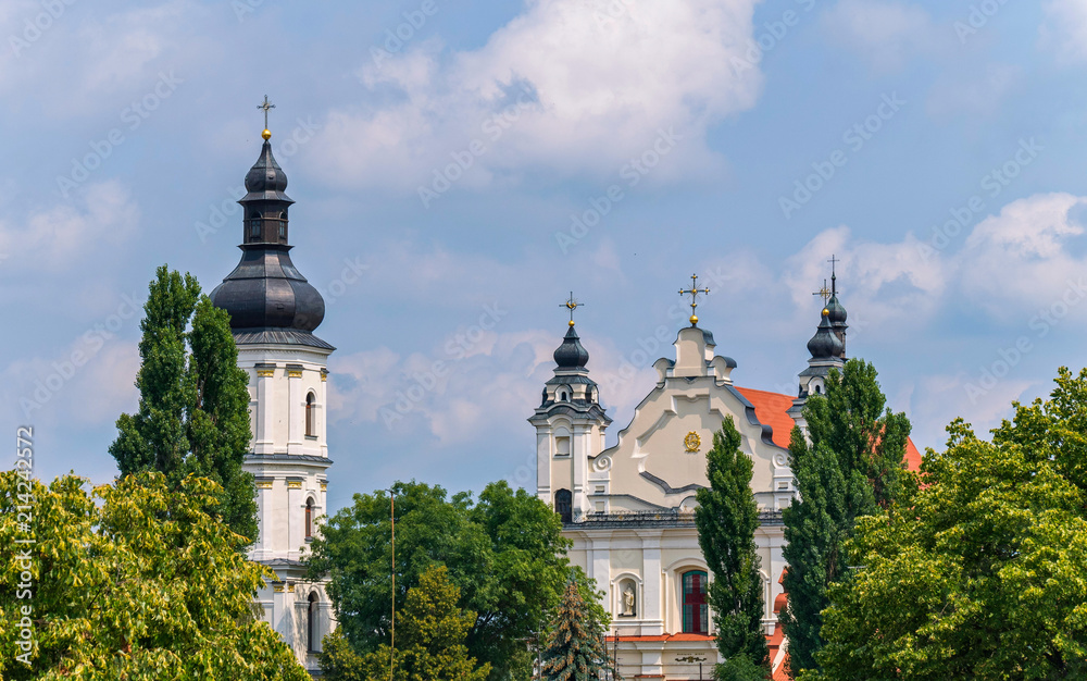 Beautiful church in classical style standing among green trees with domes and crosses on them against the sky with transparent clouds.