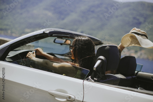Young woman with sunglasses driving her convertible top automobile on bright sunny day