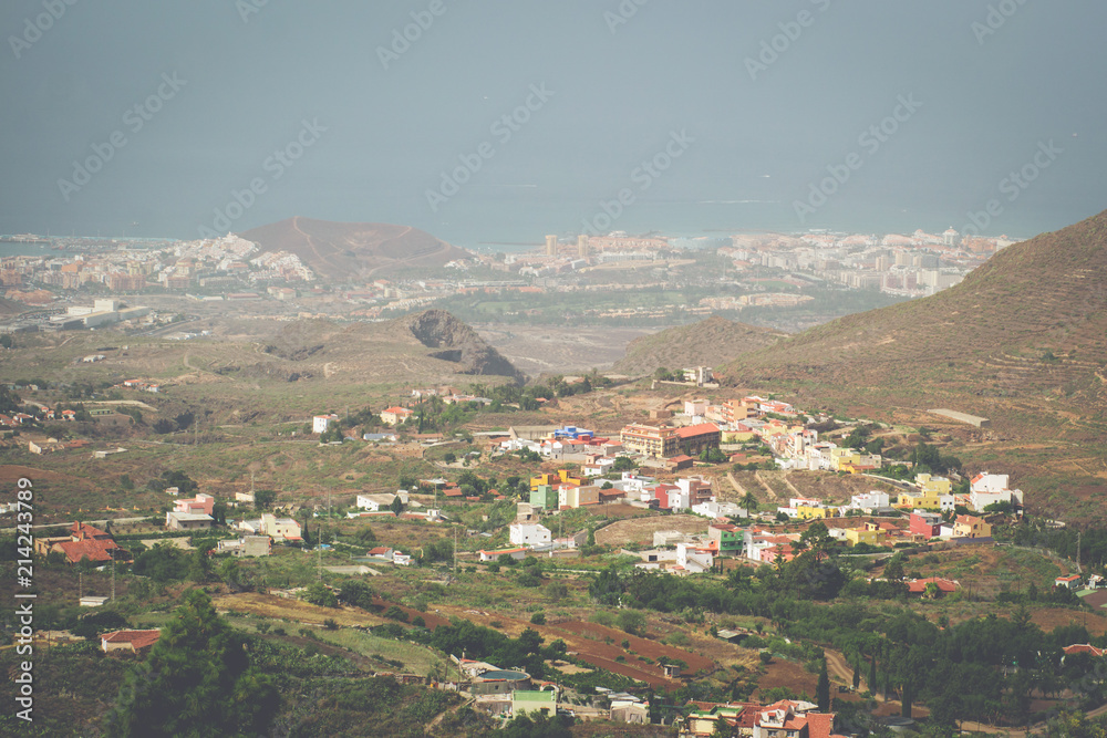 An elevated view over a Tenerife village of brightly coloured houses, the surrounding landscape and hills, the coast and ocean, all covered with the haze of La Calima (coastline of Costa Adeje)