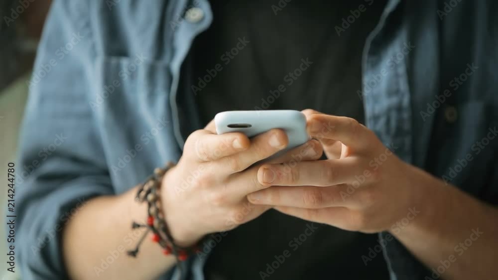 Boy texting a message on white smartphone, wearing blue shirt and black t-shirt, closeup Boy texting a message on white smartphone, wearing blue shirt and black t-shirt, closeup