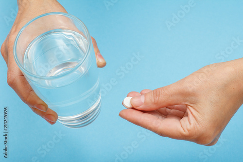 Close up hands of female patient with glass of water in one hand and white pill in another