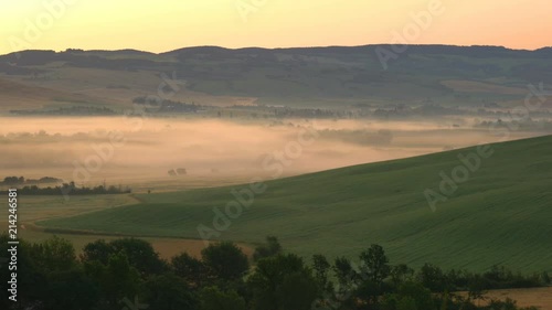 View of beautiful hilly landscape of green tuscan field with fog, line of Cypresses tree and the building at sunrise photo