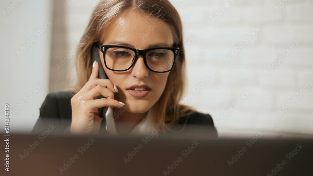 Manager doing business on phone while working at the laptop, busy smart woman dealing with customers in modern white office on typical hectic morning Manager doing business on phone while working at the laptop, busy smart woman dealing with customers in modern white office on typical hectic morning