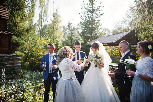 Wedding couple and groomsmen with bridesmaids drinking champagne outdoors in the park or garden.